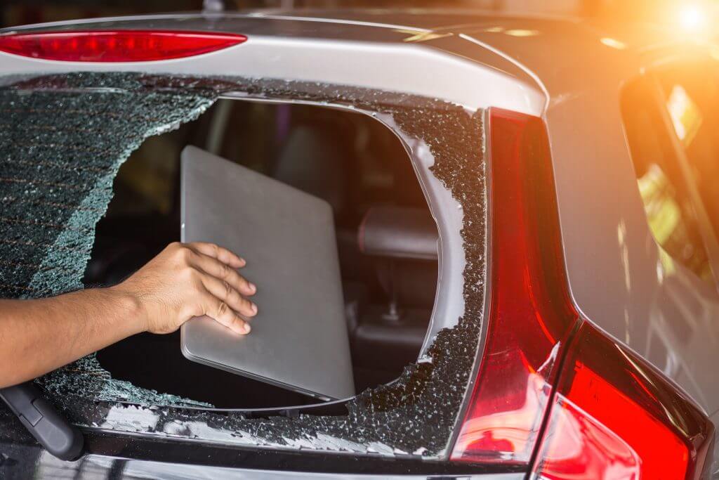 A man holding a laptop in a car window, with the reflection of the glass visible.