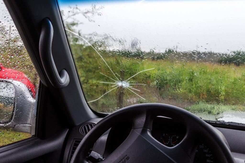 Damaged car with shattered windshield and broken side mirror.