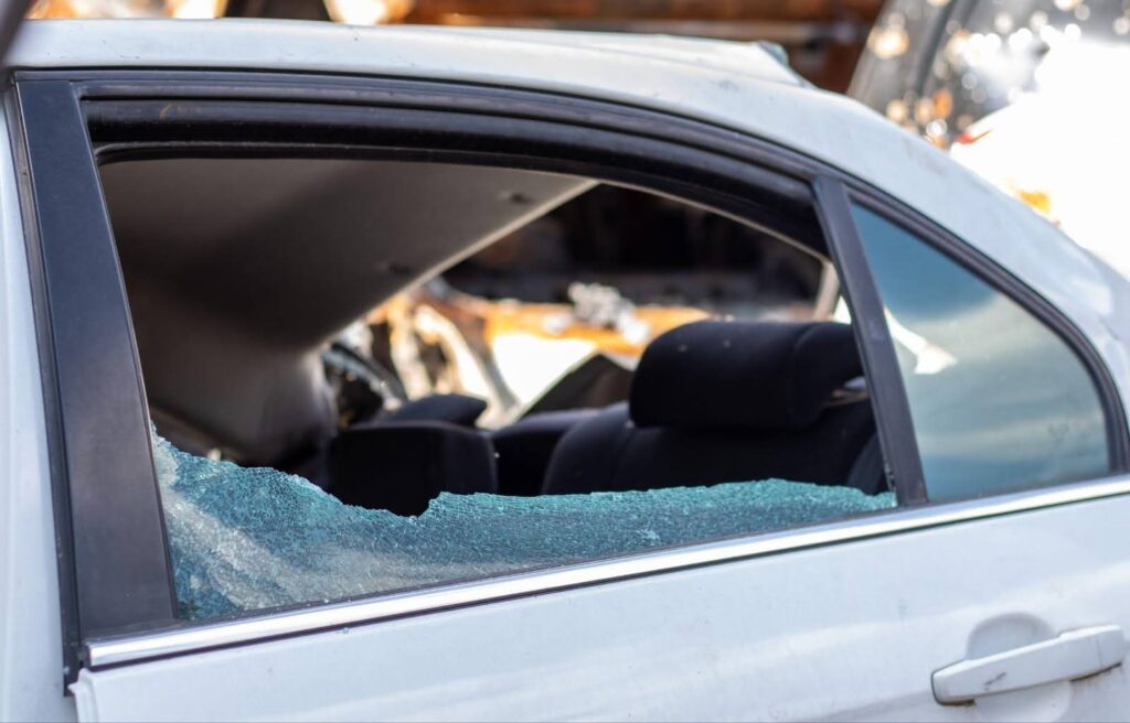 A car displaying a broken window and door, indicating potential vandalism or an unfortunate accident