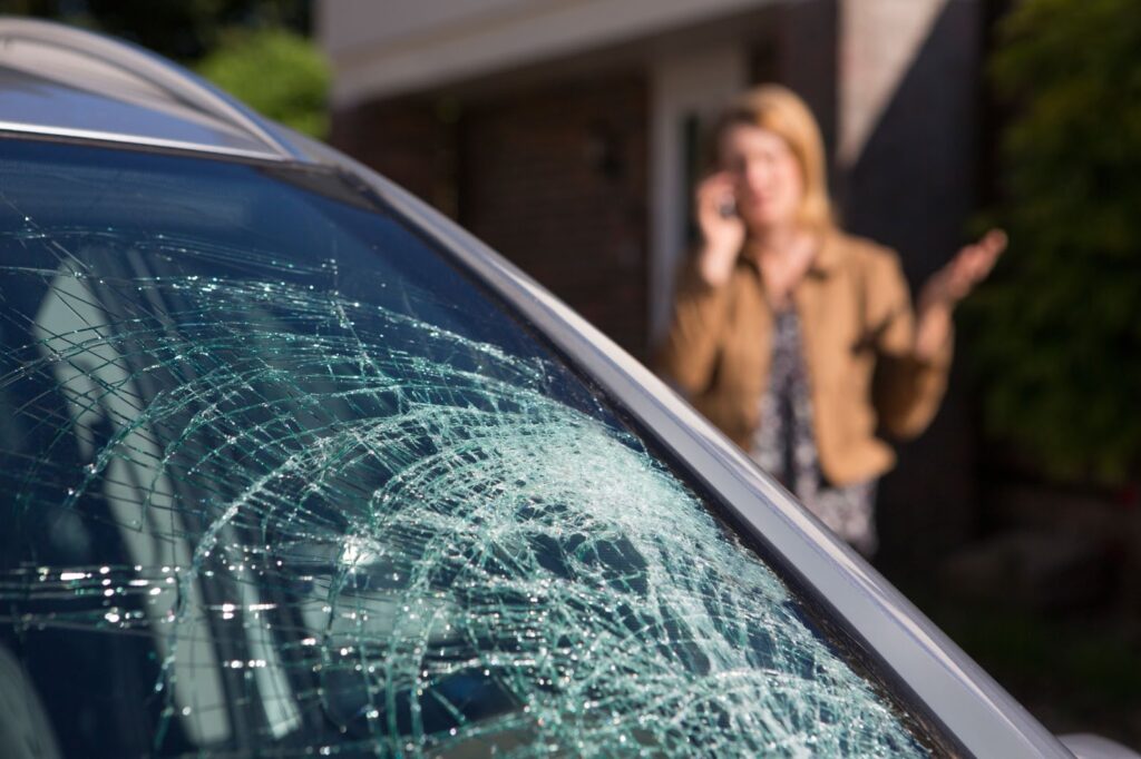 Woman next to car with shattered windshield, may need rock and chip repair or auto glass repair