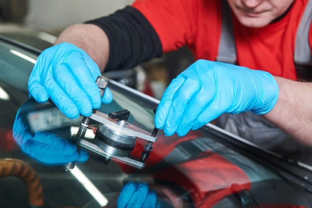 A man in a red shirt and blue gloves repairing a car windshield