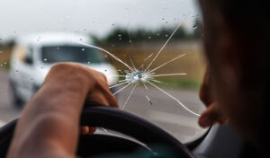 A person driving a car with a broken windshield, showcasing the need for rock chip repair services