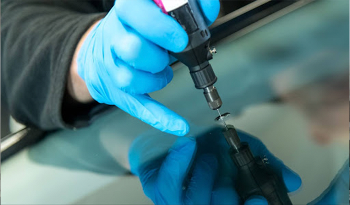 A person in blue gloves expertly uses a screwdriver to repair a windshield, focusing on a rock chip.