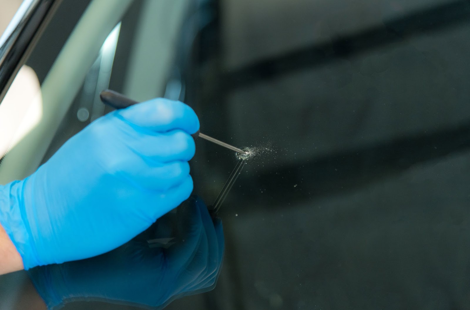 A person in blue gloves uses a tool to clean a car window.