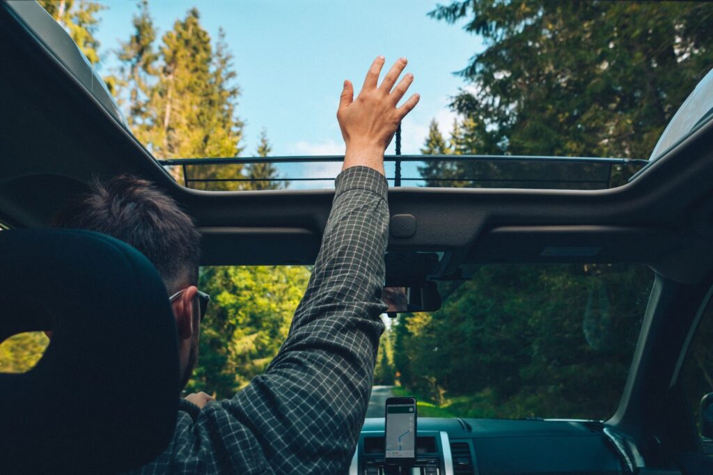 A man joyfully drives with hands up in a car with sunroof open.