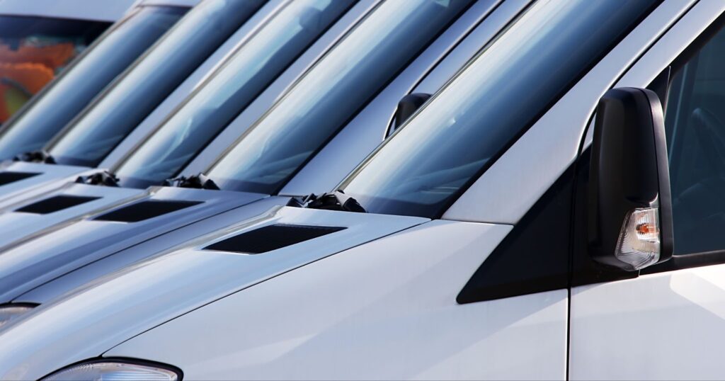 A row of white vans parked neatly, showcasing their fleet vehicle windshields ready for service and repair.