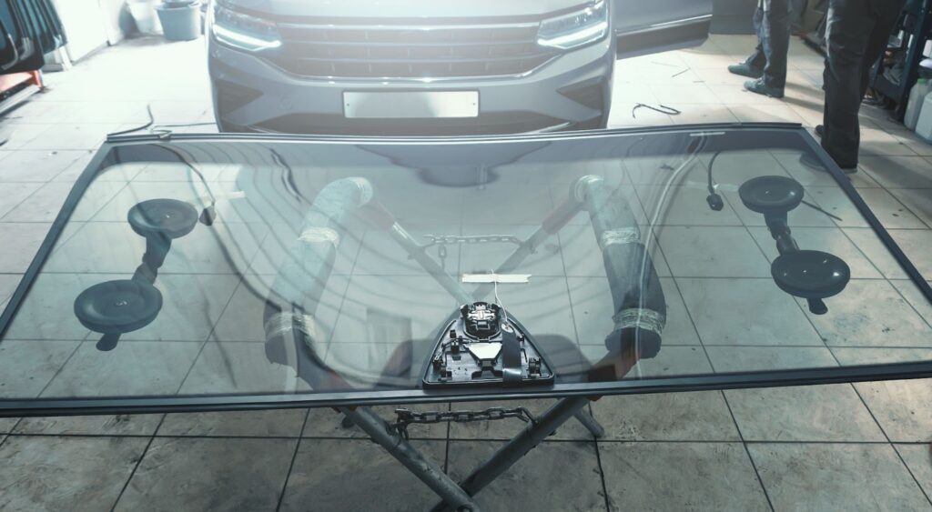 A man diligently works on a car in a garage, focusing on mobile windshield installation and automotive window replacement.