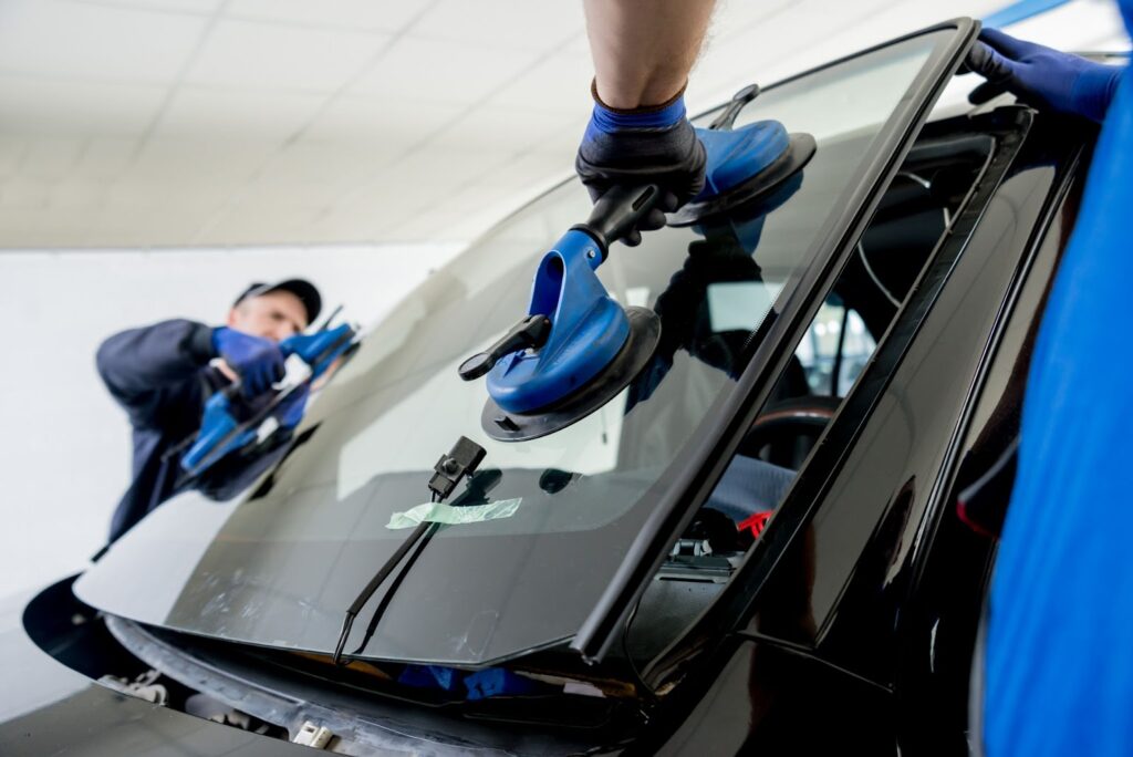 A man uses a blue tool to clean a windshield, showcasing mobile windshield installation services in action.