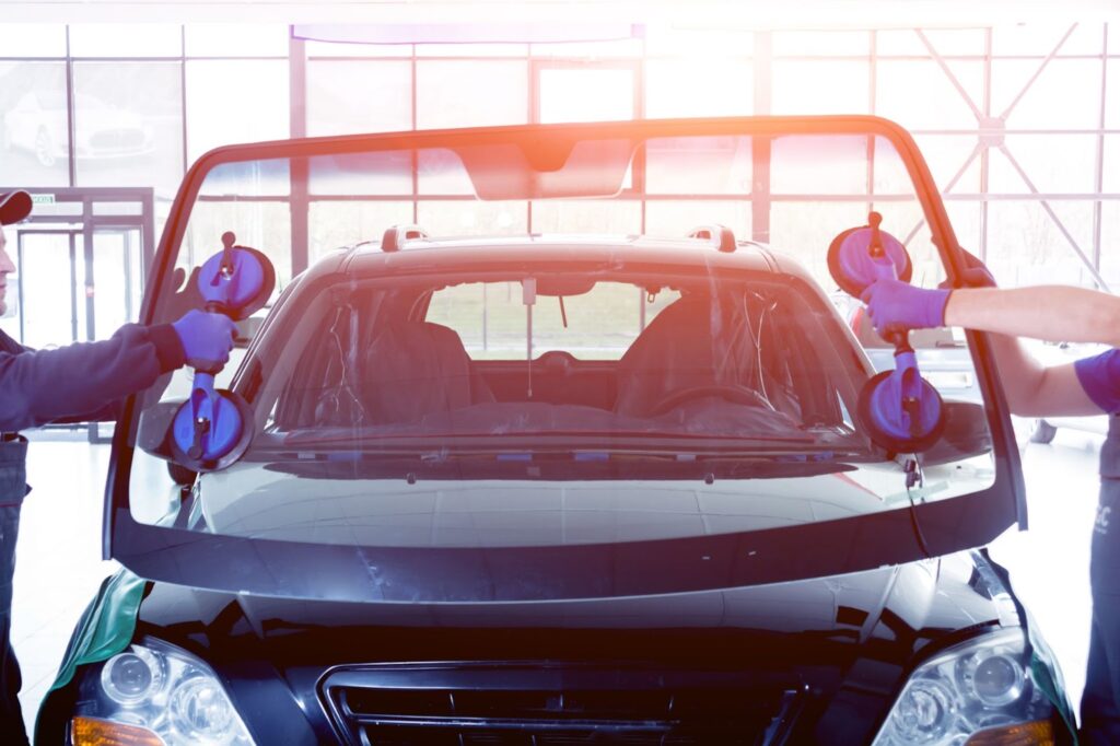 Two men in blue shirts and hats repairing a fleet vehicle's windshield in Salt Lake City.