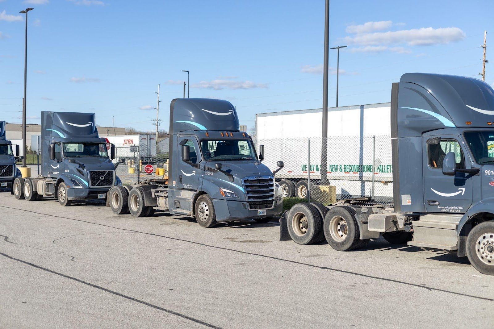 A row of semi trucks parked neatly in a spacious parking lot under clear blue skies.