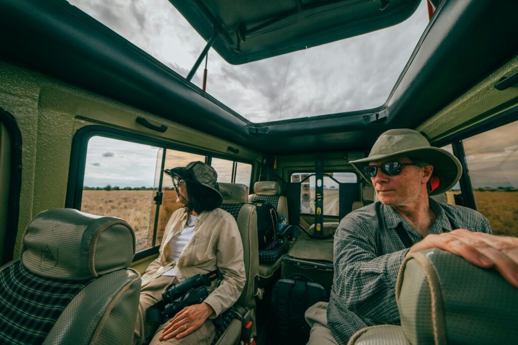 A man and woman wearing hats sit in the back of a vehicle, discussing sunroof replacement and repairs.