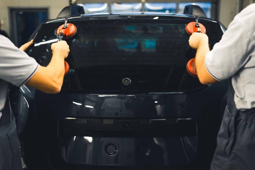 Two men are inside a car, diligently cleaning the windshield with a cloth, ensuring clear visibility