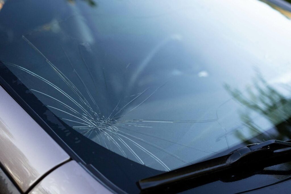 A damaged car windshield featuring extensive cracks and a prominent break, highlighting the need for repair